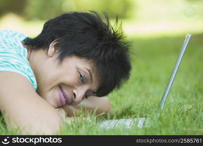 Portrait of a mature woman lying on grass with a laptop and smiling