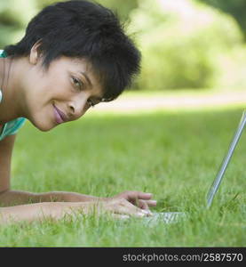 Portrait of a mature woman lying on grass with a laptop and smiling