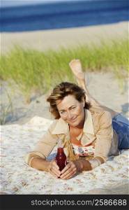 Portrait of a mature woman lying on the beach and holding a bottle
