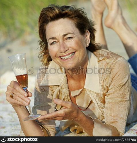 Portrait of a mature woman lying on the beach and holding a champagne flute