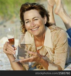Portrait of a mature woman lying on the beach and holding a champagne flute