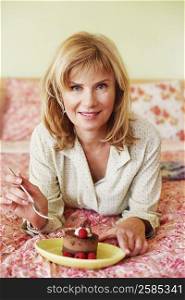 Portrait of a mature woman lying on the bed and eating cake