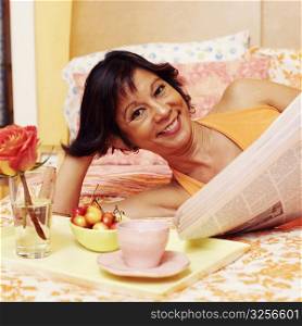Portrait of a mature woman lying on the bed and holding a newspaper
