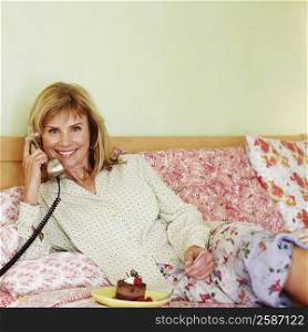 Portrait of a mature woman lying on the bed and talking on the telephone
