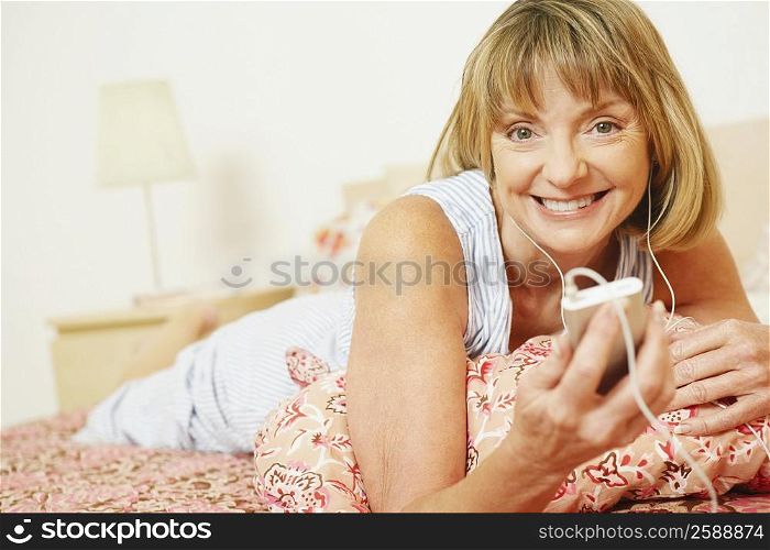 Portrait of a mature woman lying on the bed listening to an MP3 player and smiling
