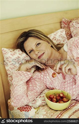 Portrait of a mature woman lying on the bed with a bowl of cherries