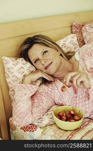 Portrait of a mature woman lying on the bed with a bowl of cherries