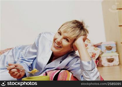 Portrait of a mature woman lying on the floor and eating corn flakes