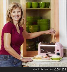 Portrait of a mature woman operating a toaster in the kitchen and smiling