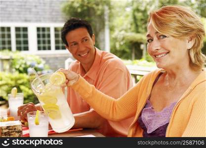 Portrait of a mature woman pouring lemon juice in a glass with a mature man sitting beside her