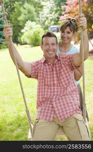 Portrait of a mature woman pushing a mature man on a rope swing and smiling