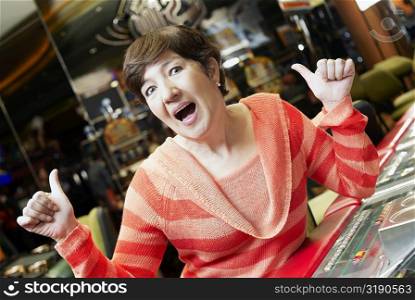 Portrait of a mature woman showing a thumbs up sign sitting in front of a slot machine