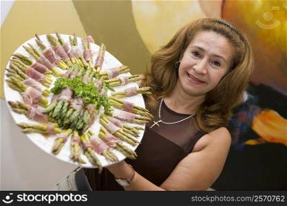 Portrait of a mature woman showing prosciutto wrapped asparagus arranged in a plate