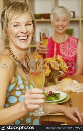 Portrait of a mature woman sitting at the dining table with her friend and holding a champagne flute