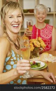 Portrait of a mature woman sitting at the dining table with her friend and holding a champagne flute