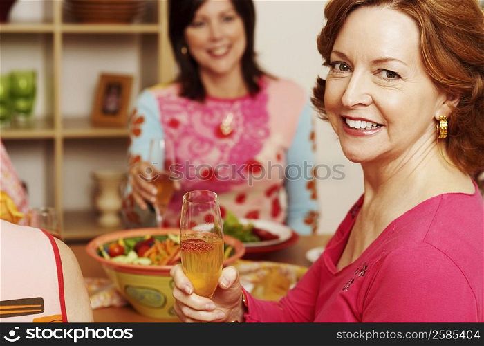 Portrait of a mature woman sitting at the dining table with her friend holding a champagne flute