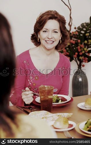 Portrait of a mature woman sitting at the dining table with her friend and smiling