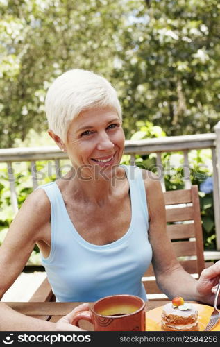 Portrait of a mature woman sitting at the table with a plate of dessert in front of her and smiling
