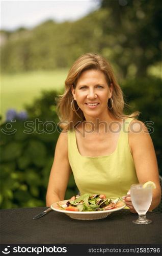 Portrait of a mature woman sitting at the table with a plate of vegetable salad in front of her