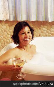 Portrait of a mature woman sitting in a bathtub and holding a glass of wine