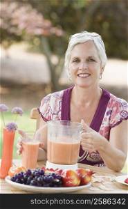 Portrait of a mature woman sitting in a lawn and holding a blender filled with juice