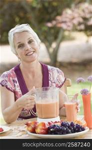 Portrait of a mature woman sitting in a lawn and holding a blender filled with juice