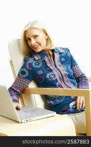 Portrait of a mature woman sitting in an armchair and using a laptop