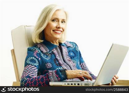 Portrait of a mature woman sitting in an armchair and using a laptop