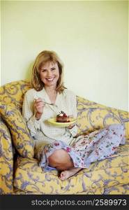 Portrait of a mature woman sitting on a couch and eating cake