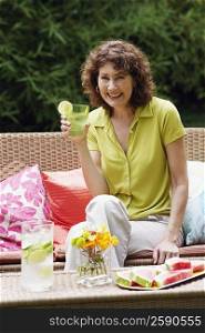 Portrait of a mature woman sitting on a couch and holding a glass of lemonade
