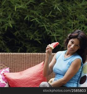 Portrait of a mature woman sitting on a couch and holding a slice of watermelon