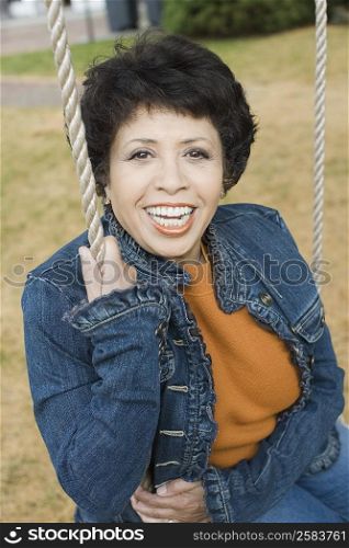 Portrait of a mature woman sitting on a rope swing and smiling