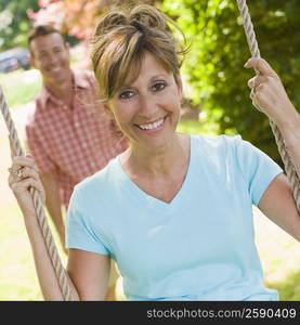 Portrait of a mature woman sitting on a rope swing with a mature man standing in the background