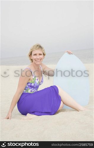 Portrait of a mature woman sitting on the beach holding a body board and smiling