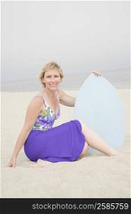 Portrait of a mature woman sitting on the beach holding a body board and smiling