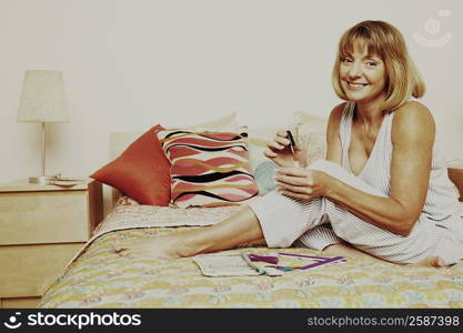 Portrait of a mature woman sitting on the bed and holding a nail polish