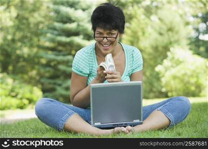 Portrait of a mature woman sitting with a laptop and holding a wad of currency