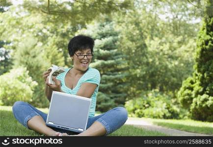 Portrait of a mature woman sitting with a laptop and holding a wad of currency