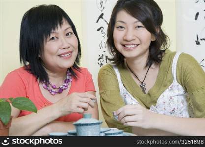 Portrait of a mature woman sitting with her daughter at a table and holding tea cups