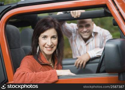 Portrait of a mature woman smiling in a jeep with a mid adult man in the background