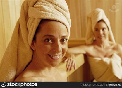 Portrait of a mature woman smiling with another woman sitting behind her in a sauna