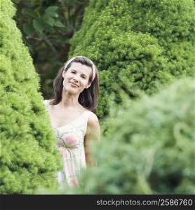 Portrait of a mature woman standing behind a hedge and smiling