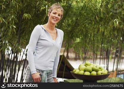 Portrait of a mature woman standing beside a bowl of apples