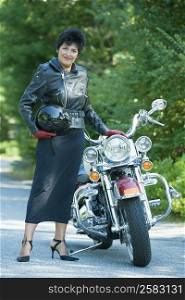 Portrait of a mature woman standing beside a motorcycle and holding a crash helmet