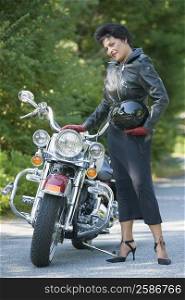 Portrait of a mature woman standing beside a motorcycle and holding a crash helmet