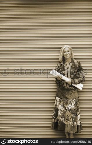 Portrait of a mature woman standing in front of a shutter and holding rolls of paper
