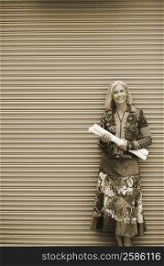 Portrait of a mature woman standing in front of a shutter and holding rolls of paper