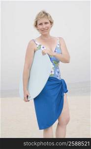 Portrait of a mature woman standing on the beach and holding a body board