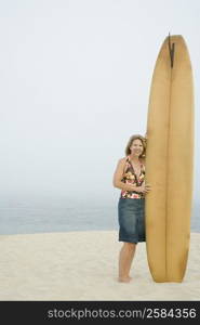 Portrait of a mature woman standing with a surfboard on the beach