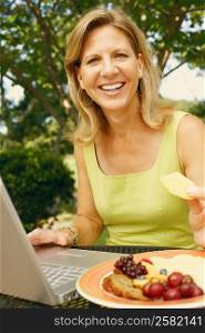 Portrait of a mature woman using a laptop and eating fruit salad